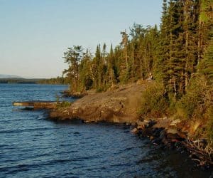 A lone camper sitting near the dock at Three Mile campsite at the edge of Rock Harbor, on Isle Royale. © 2002 Todd VerBeek.